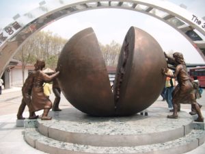 Photo of statue at DMZ, people pushing two halves of a ball together